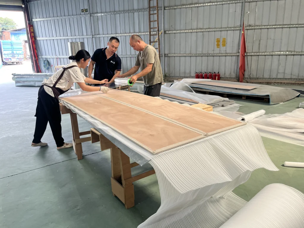 Saipin Decor factory workers applying multi-layered protective packaging to custom upholstered wall panels for international shipping.