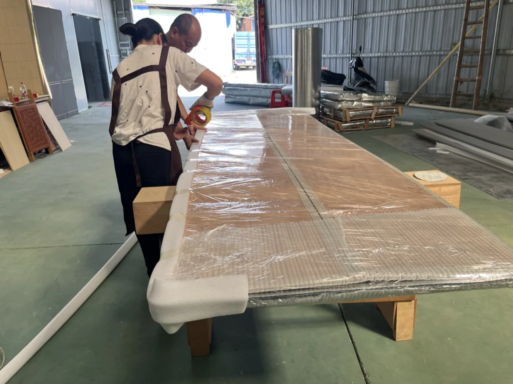 Saipin Decor factory workers applying multi-layered protective packaging to custom upholstered wall panels for international shipping.