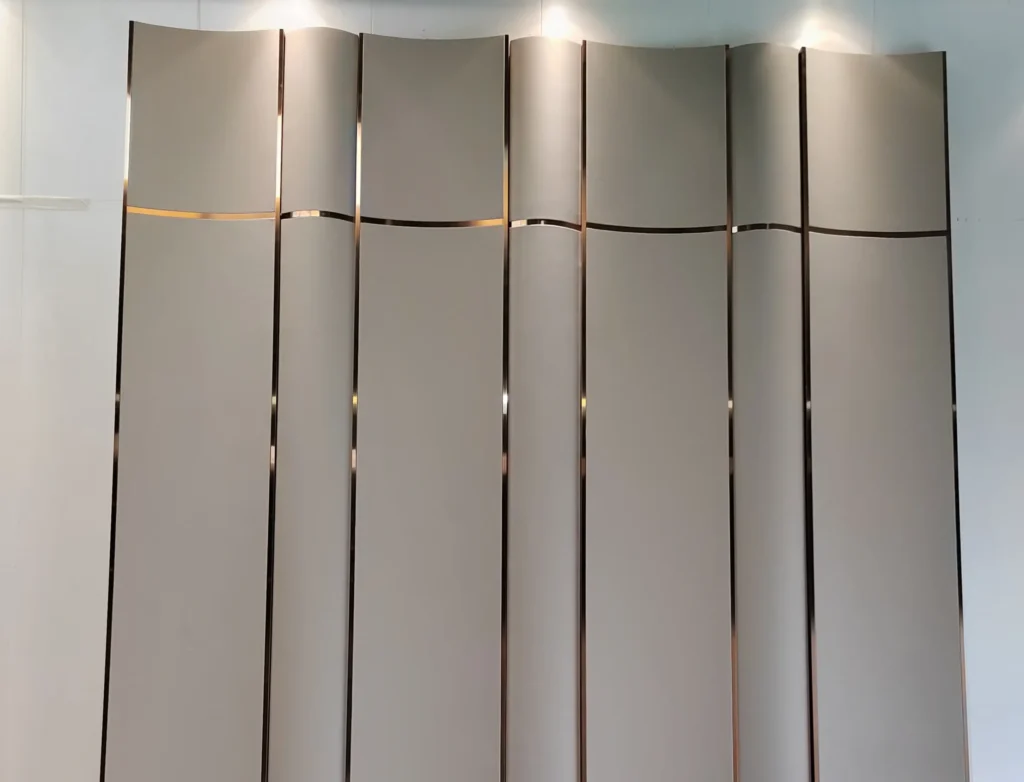 factory production floor showing Saipin Decor's bespoke 3D curved upholstered wall panels in matte taupe, featuring flawless integration of straight vertical and wavy horizontal brass metal inlays.