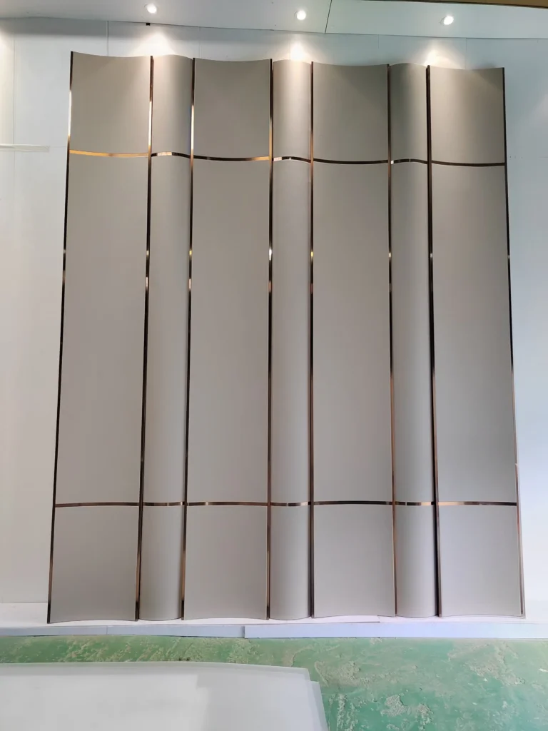 actory production floor showing Saipin Decor's bespoke 3D curved upholstered wall panels in matte taupe, featuring flawless integration of straight vertical and wavy horizontal brass metal inlays.