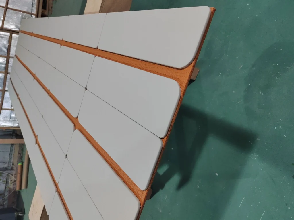 Large-scale custom two-tone upholstered wall panels laid out on the Saipin Decor factory floor, featuring light grey pads over a textured orange base.