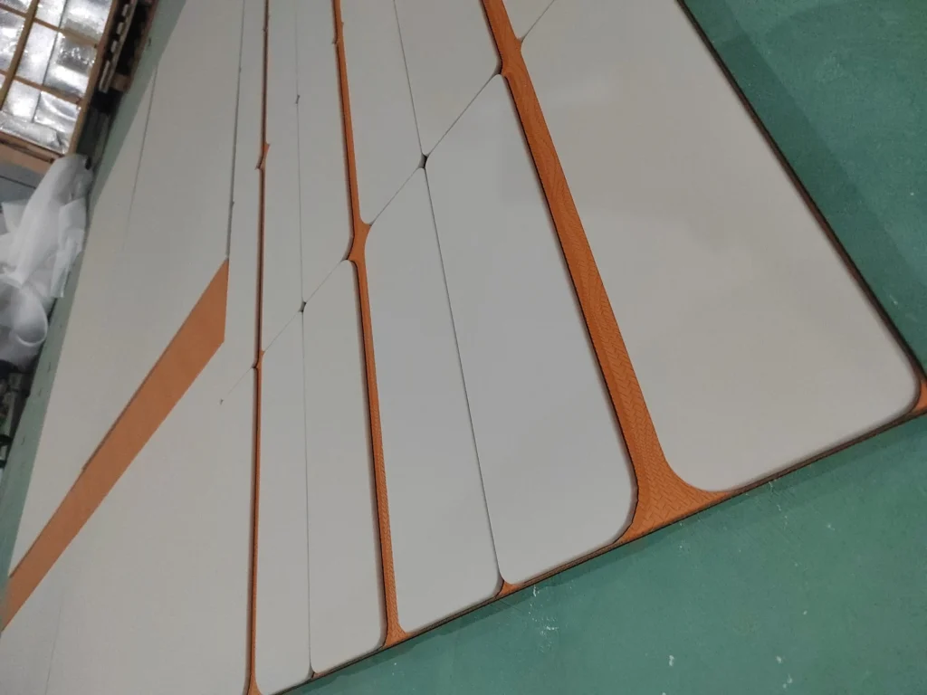 Large-scale custom two-tone upholstered wall panels laid out on the Saipin Decor factory floor, featuring light grey pads over a textured orange base.