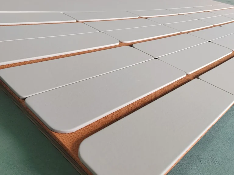 Large-scale custom two-tone upholstered wall panels laid out on the Saipin Decor factory floor, featuring light grey pads over a textured orange base.