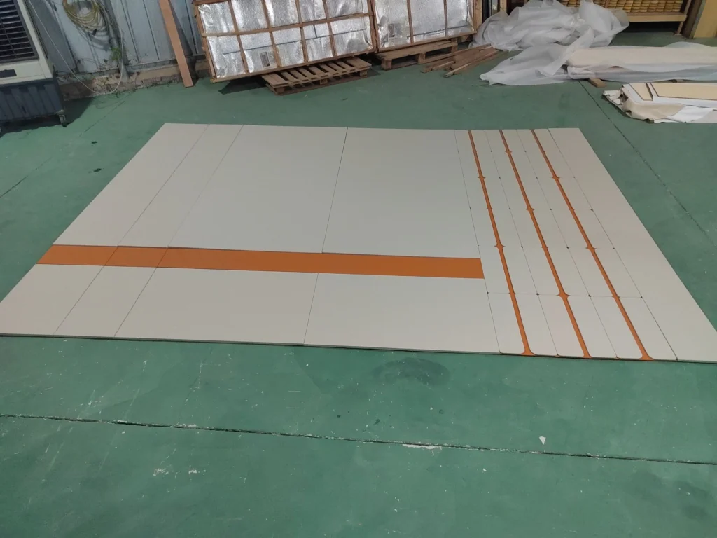 Large-scale custom two-tone upholstered wall panels laid out on the Saipin Decor factory floor, featuring light grey pads over a textured orange base.